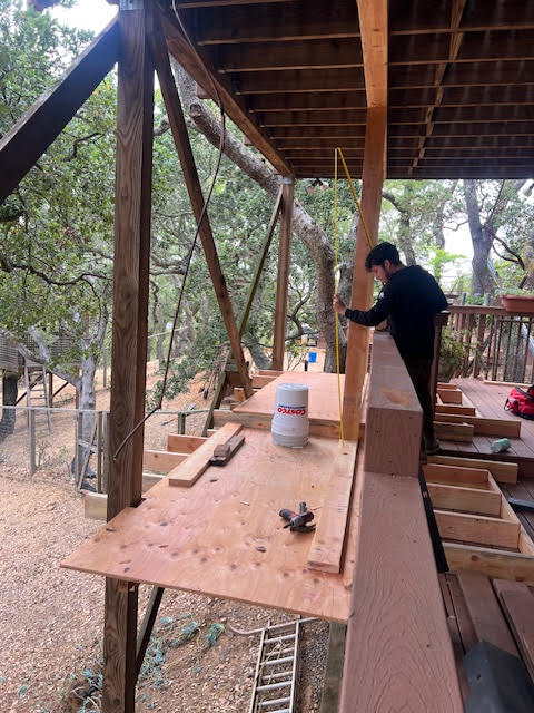 Person working on a wooden structure with trees in the background
