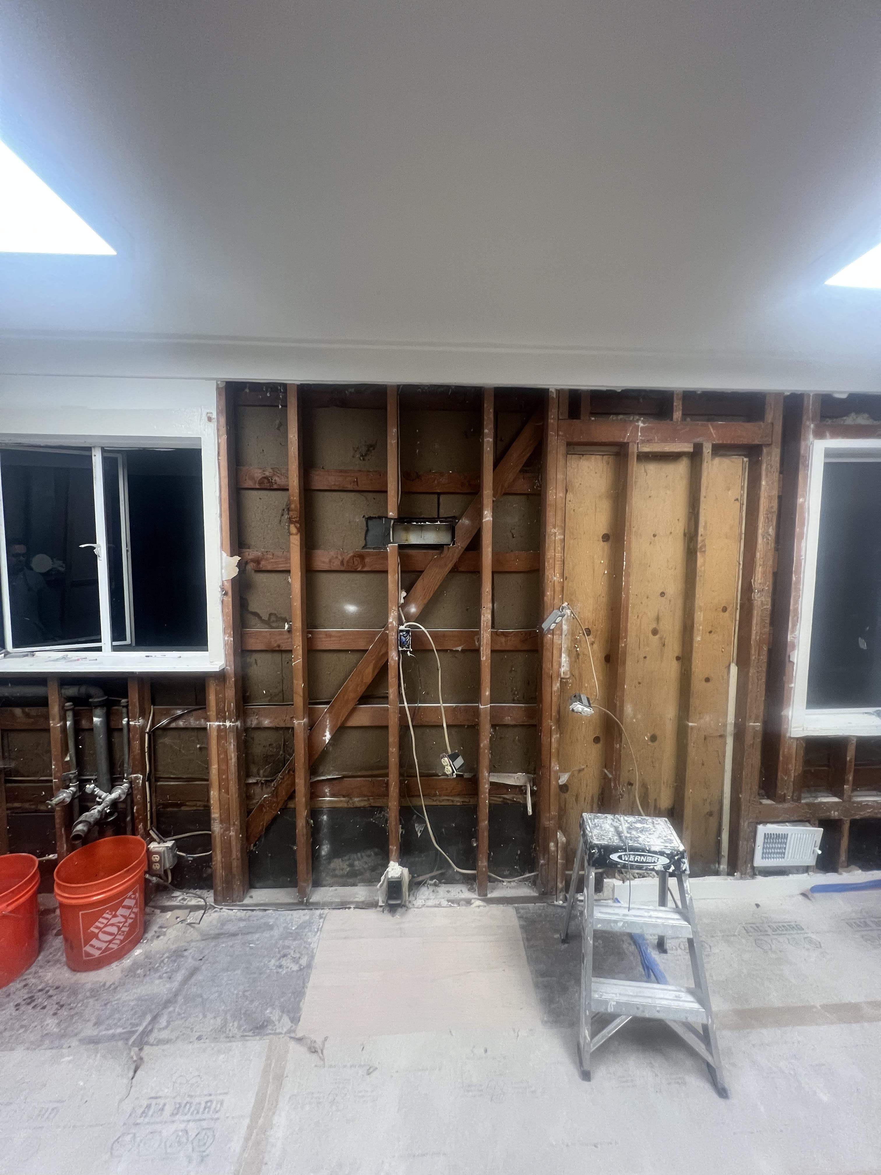 Room under construction with exposed wooden beams and wiring, ladder, and buckets.