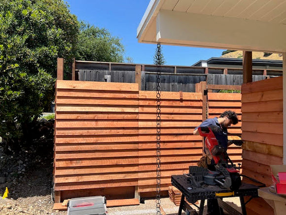 Person working on a wooden fence installation with tools in a backyard setting.