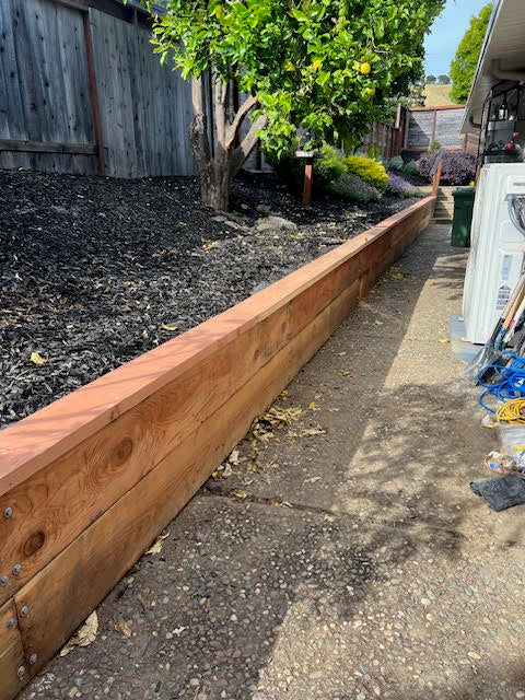 Wooden retaining wall in a backyard with mulch and a tree